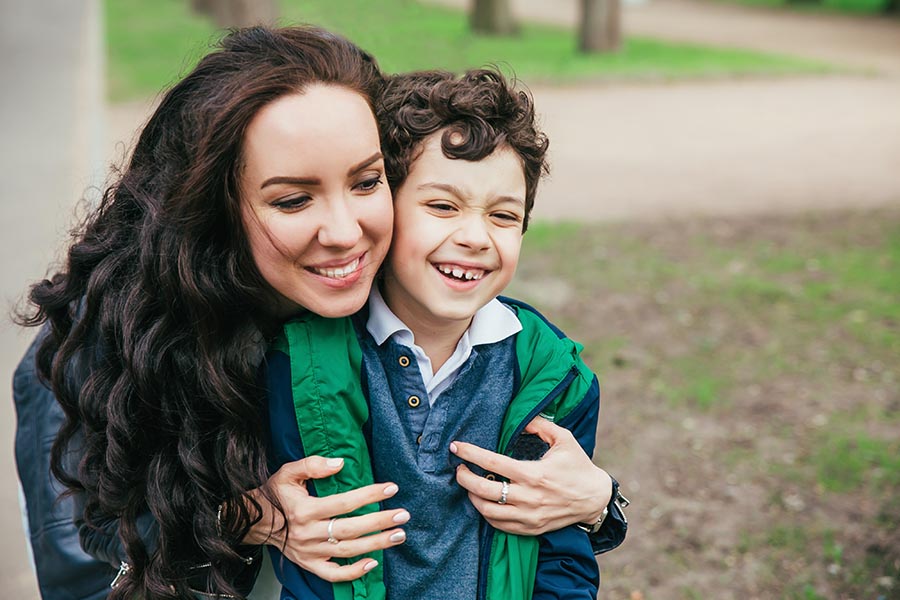 Personal Insurance - Mother With Long Dark Hair Smiles and Hugs Her Young Son Who Laughs and Looks Embarrassed